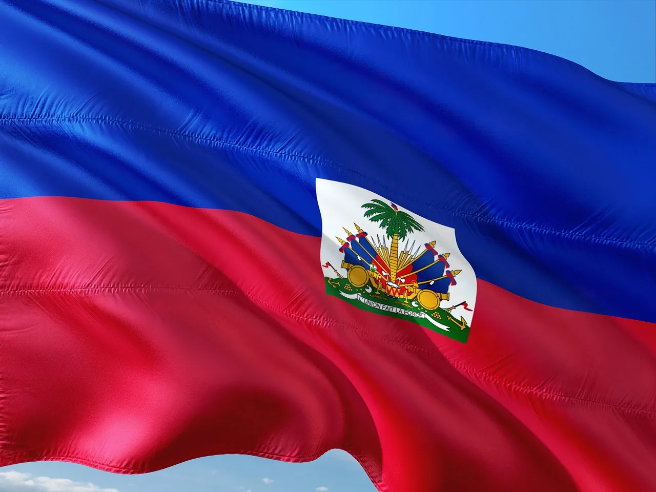 Bandera de Haití ondeando contra un cielo azul, con el escudo nacional en el centro.