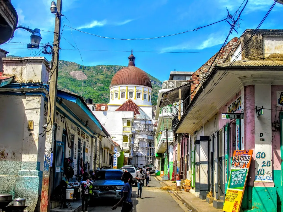 Calle de Cabo Haitiano con casas de colores y la cúpula de la catedral al fondo, entre montañas.